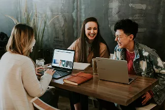 Three women seated at a table, each using a laptop, engaged in discussion and collaboration