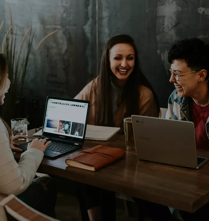Three women seated at a table, each using a laptop, engaged in discussion and collaboration
